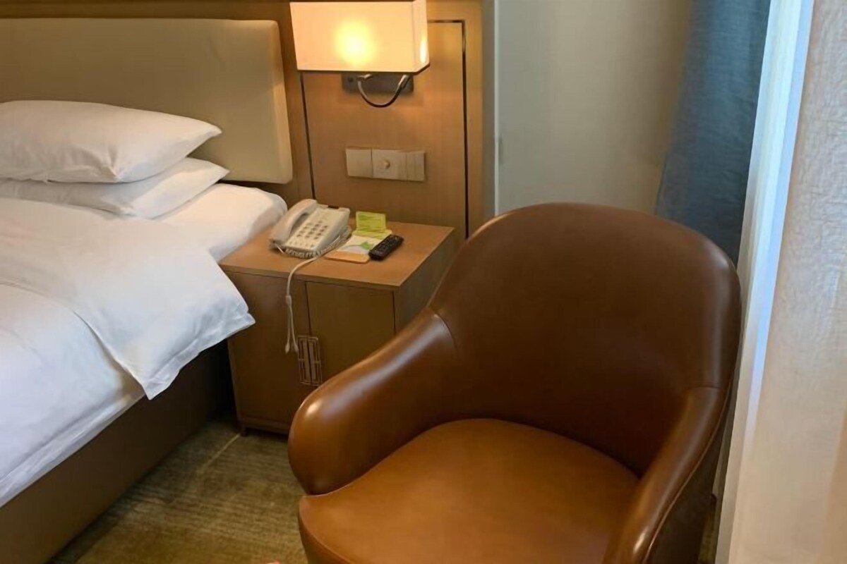 Una habitación de hotel con una cama, una mesita de noche con lámpara, un teléfono y un sillón de cuero marrón.