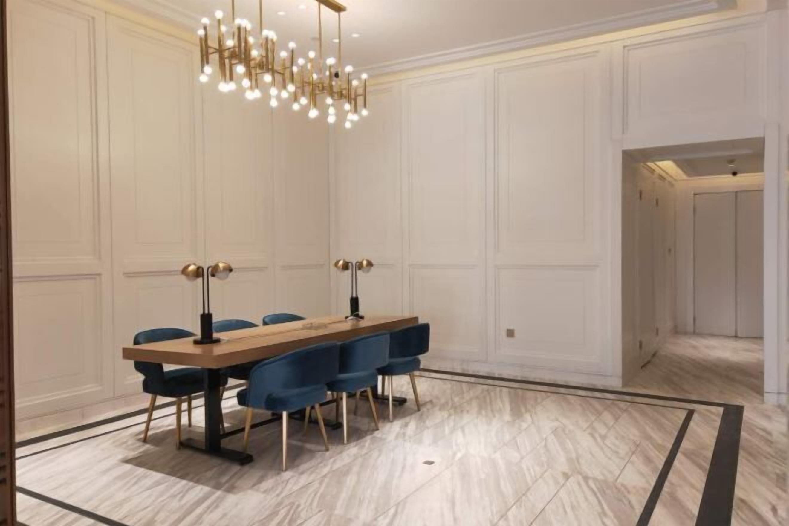 A dining area with a long wooden table, blue chairs, and a modern chandelier.