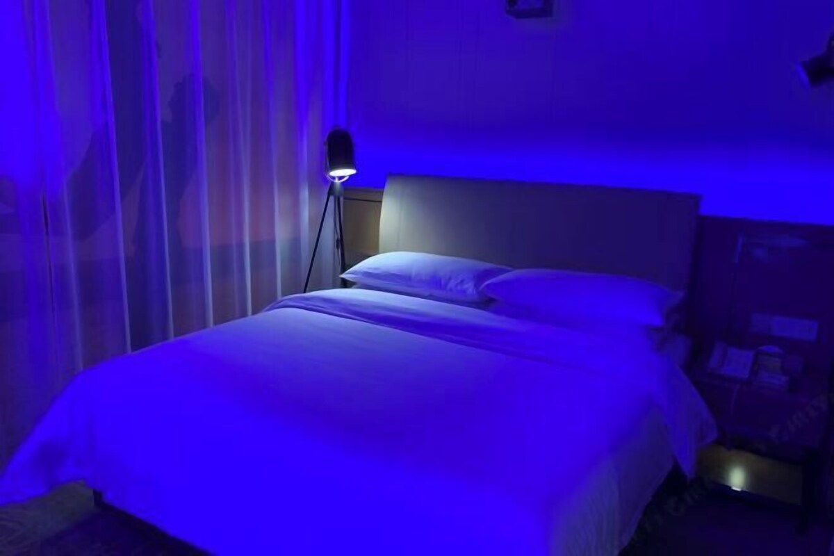 Una cama con cabecera, una lámpara de noche y una cortina.