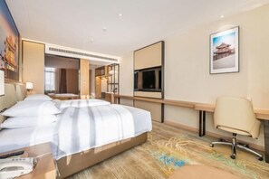 Habitación de hotel con cama, escritorio, silla, televisión y un cuadro en la pared.