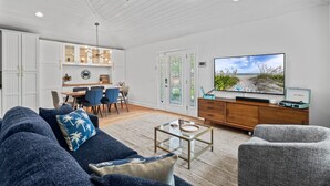 A spacious living room with a large TV, a ceiling fan, and a dining area with chairs and a table. - Endless Summer Retreat (Jacksonville Beach)