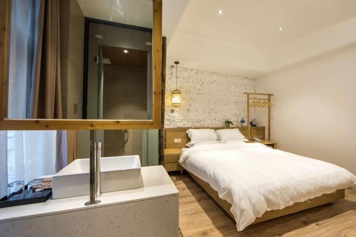 A modern hotel room with a large bed, a bedside table, a mirror, and a shower area.