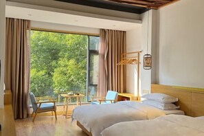Habitació d'hotel amb dos llits, una taula de treball, una cadira i una finestra gran amb cortines.