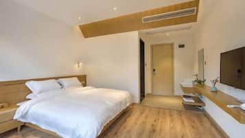 A modern hotel room with a wooden bed, a bedside table, a built-in desk with a mirror, and a small plant.
