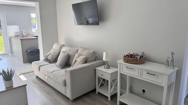 En moderne stue med en grå sofa, et hvidt sengebord, et tv ophængt på væggen og et lille hvidt skrivebord med skuffer.