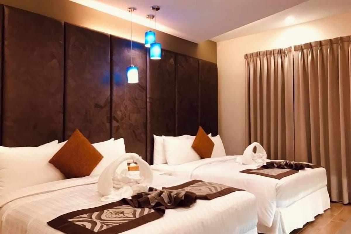 A hotel room with two beds, a large dark headboard, a curtain, and a blue pendant light.