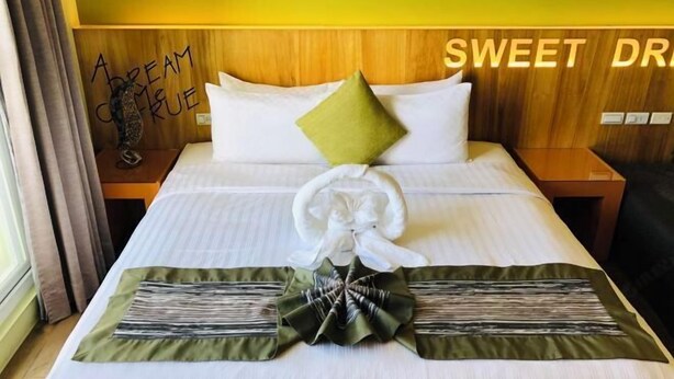 A neatly made bed with a green and white pillow, a white pillow, and a decorative bow on the bedspread. - Baishatan Hotel (Hengchun)
