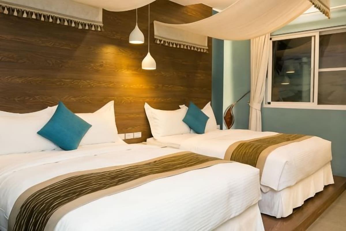 A hotel room with two beds, a wooden headboard, a window, and a hanging light fixture.