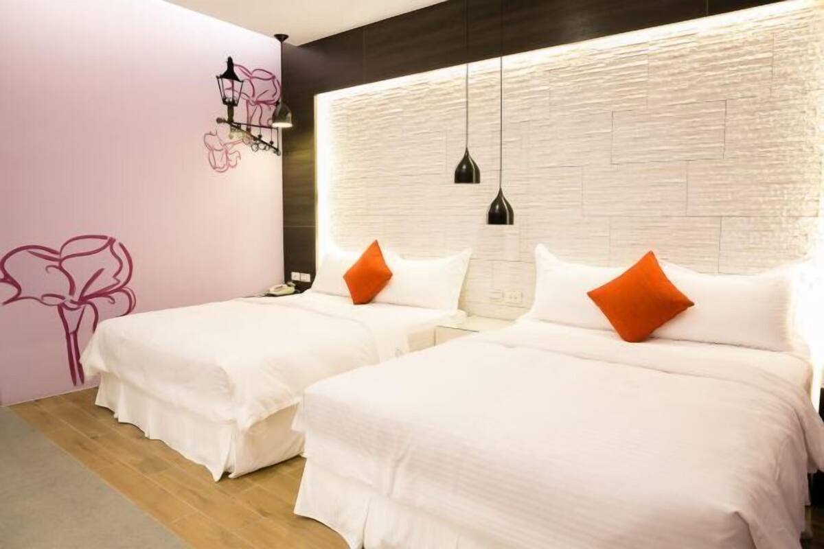 Habitación de hotel con dos camas, una pared blanca con textura y otra pared rosa con diseño floral.
