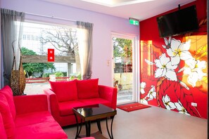 A hotel lobby with a red sofa, a small table, and a wall with a floral mural.
