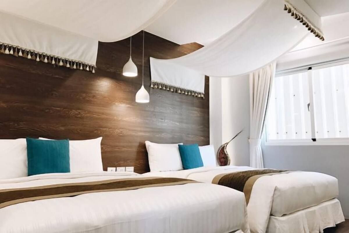 Habitación de hotel moderna con dos camas, ropa de cama blanca y cabecero de madera.