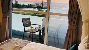 A hotel room with a bed, a chair, a small table, and a view of the cityscape through large windows. - Baishatan Hotel (Hengchun)