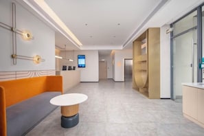 A modern hotel lobby with a reception desk, seating area, and a digital screen.