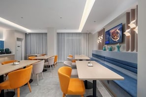 A modern dining area with tables and chairs, a blue bench, and a wall-mounted TV.