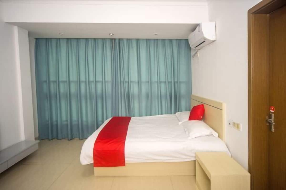 Ein Hotelzimmer mit einem Bett, einem Nachttisch, einem Fenster mit Vorhängen und einer Klimaanlage.