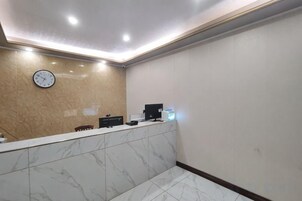 Zona de recepción con mostrador de mármol, un reloj y un monitor de computadora.