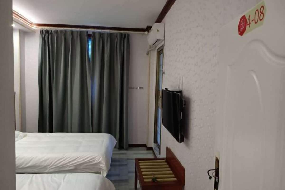 Ein Hotelzimmer mit zwei Betten, einem an der Wand montierten Fernseher und einem Fenster mit Vorhängen.