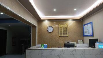 A reception area with a marble counter, a clock, a bulletin board, and a framed notice on the wall.