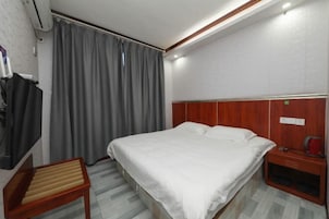 Habitación de hotel con cama, mesita de noche de madera, una silla, un armario y una cortina.