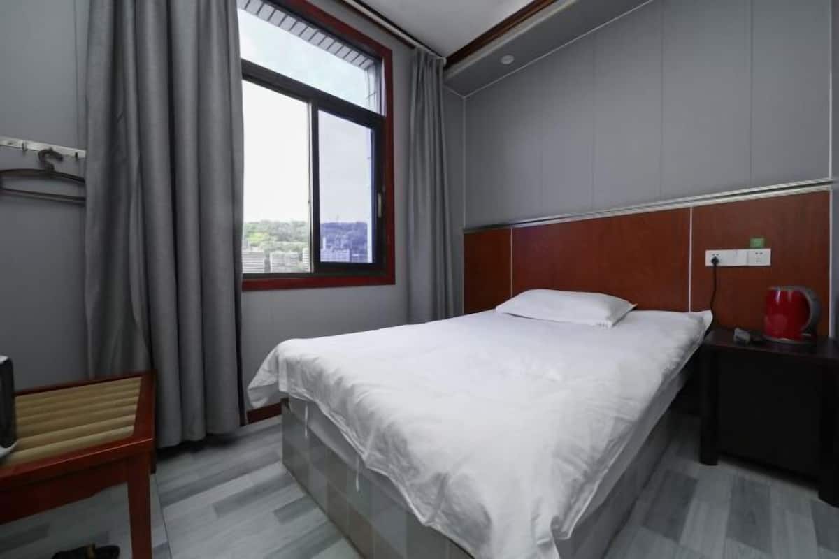 Ein Hotelzimmer mit einem Bett, einem Nachttisch, einem Fernseher und einem Fenster mit Vorhängen.