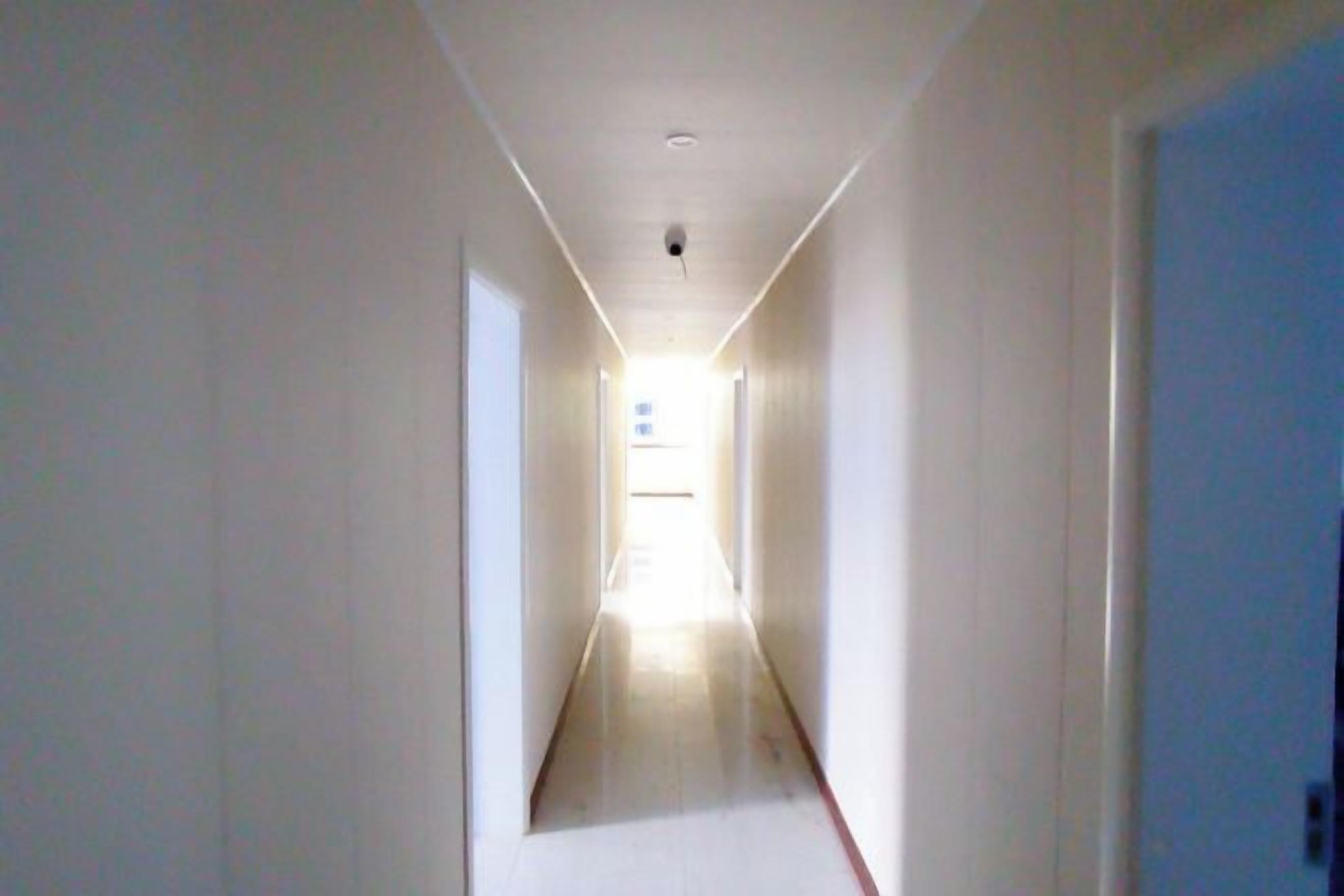 A narrow hallway with a light source at the end, leading to a door.