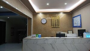 Un espace d’accueil comprenant un comptoir en marbre, une horloge, un tableau d’affichage et un écran d’ordinateur.