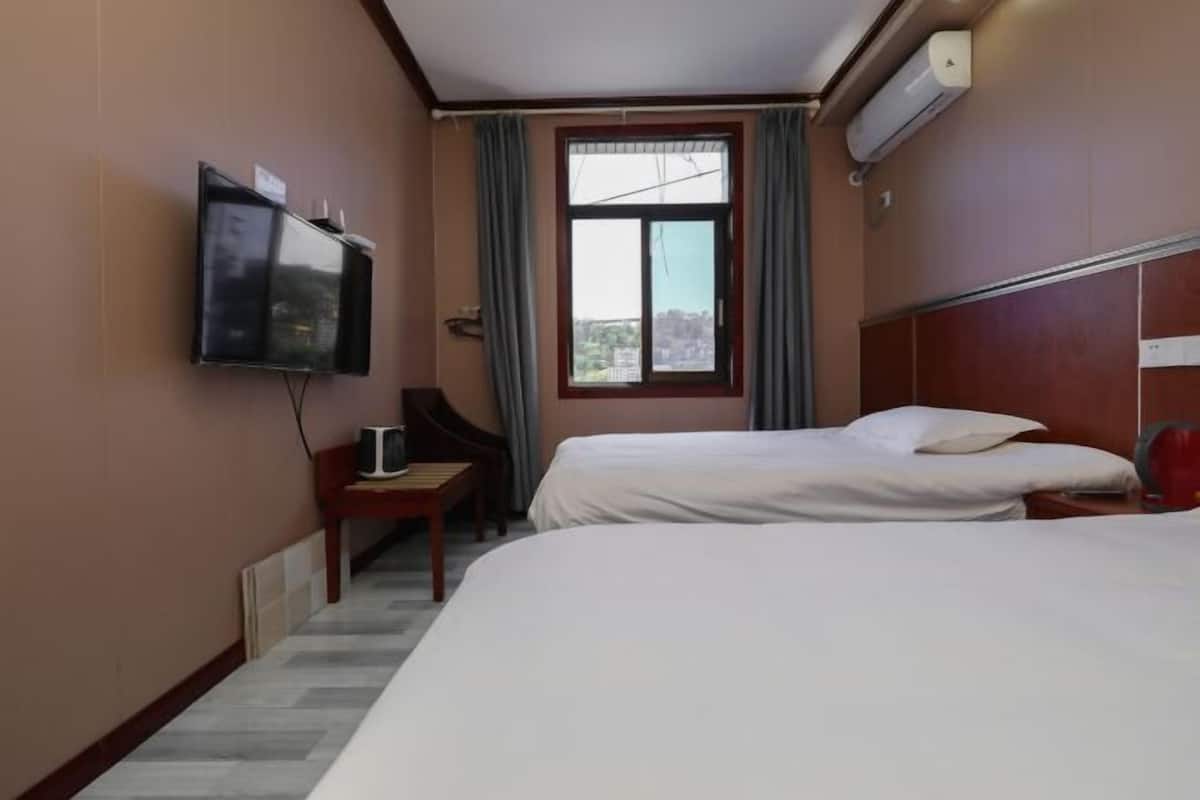 Ein Hotelzimmer mit zwei Betten, einem Fernseher, einem Schreibtisch und einem fenster mit Vorhängen.