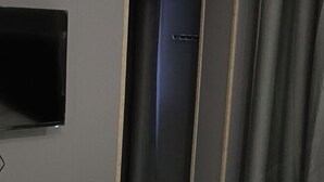 Une pièce dotée d’un téléviseur à écran plat fixé au mur, d’une porte avec une poignée et d’un rideau.