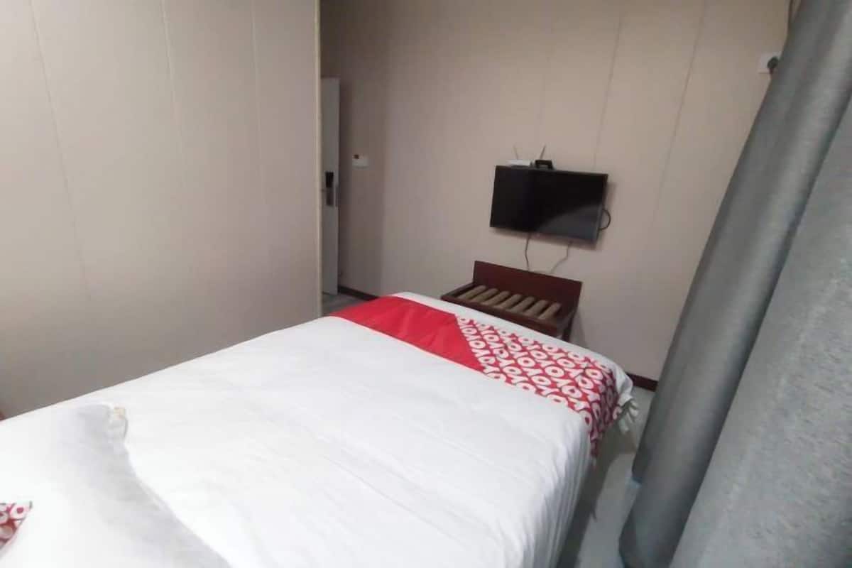 Ein Hotelzimmer mit Bett, Wandfernseher und Vorhang am Fenster.