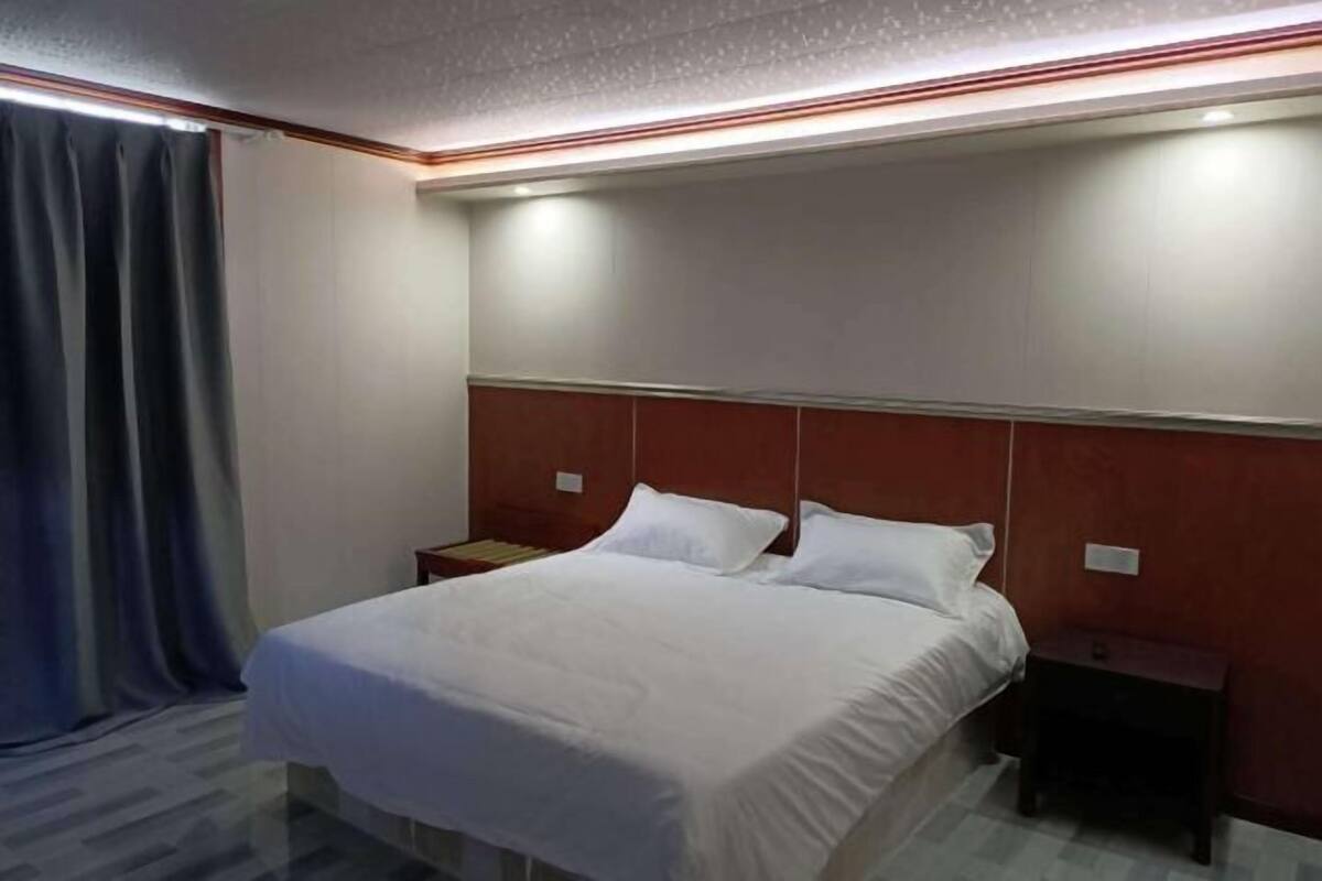 Ein Hotelzimmer mit Bett, zwei Nachttischen, einem Kopfteil und einem Vorhang.