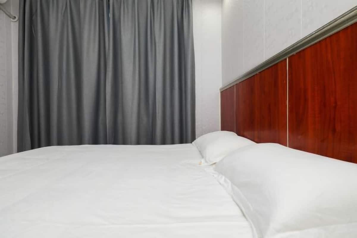 Ein ordentlich bezogenes Bett mit weißen Leinen in einem Raum, der ein Holz-Kopfteil und graue Vorhänge hat.