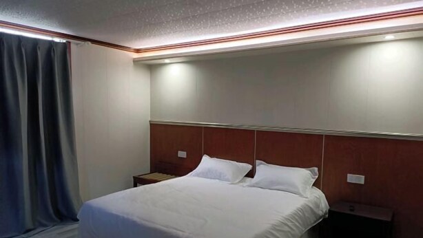 Une chambre d’hôtel avec un lit, deux tables de chevet, une tête de lit et un rideau.