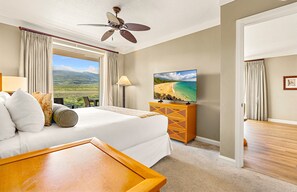 Ein Hotelzimmer mit einem Bett, einem Fernseher, einem Deckenventilator und Blick auf einen Strand.