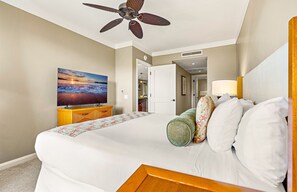 Ein Hotelzimmer mit einem Bett, einem Fernseher, einem Deckenventilator und einer Tür zu einem weiteren Raum.
