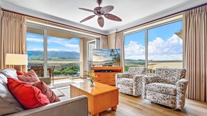 Un salón amplio con un televisor de pantalla plana grande, asientos cómodos y vistas a un paisaje pintoresco a través de grandes ventanales.