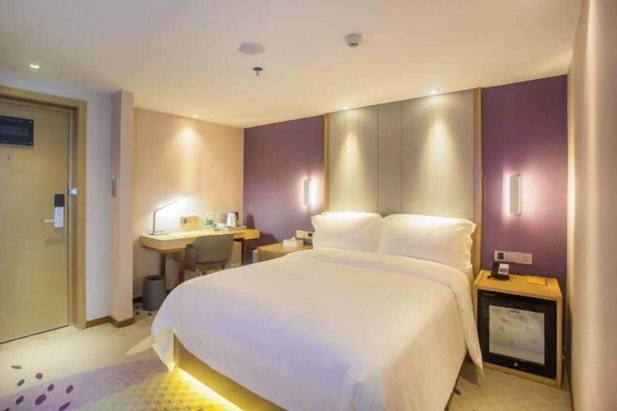 Ein Hotelzimmer mit einem großen Bett, einem Schreibtisch mit Stuhl, einem kleinen Tisch mit Lampe und einem Nachttisch mit Telefon und Bilderrahmen.