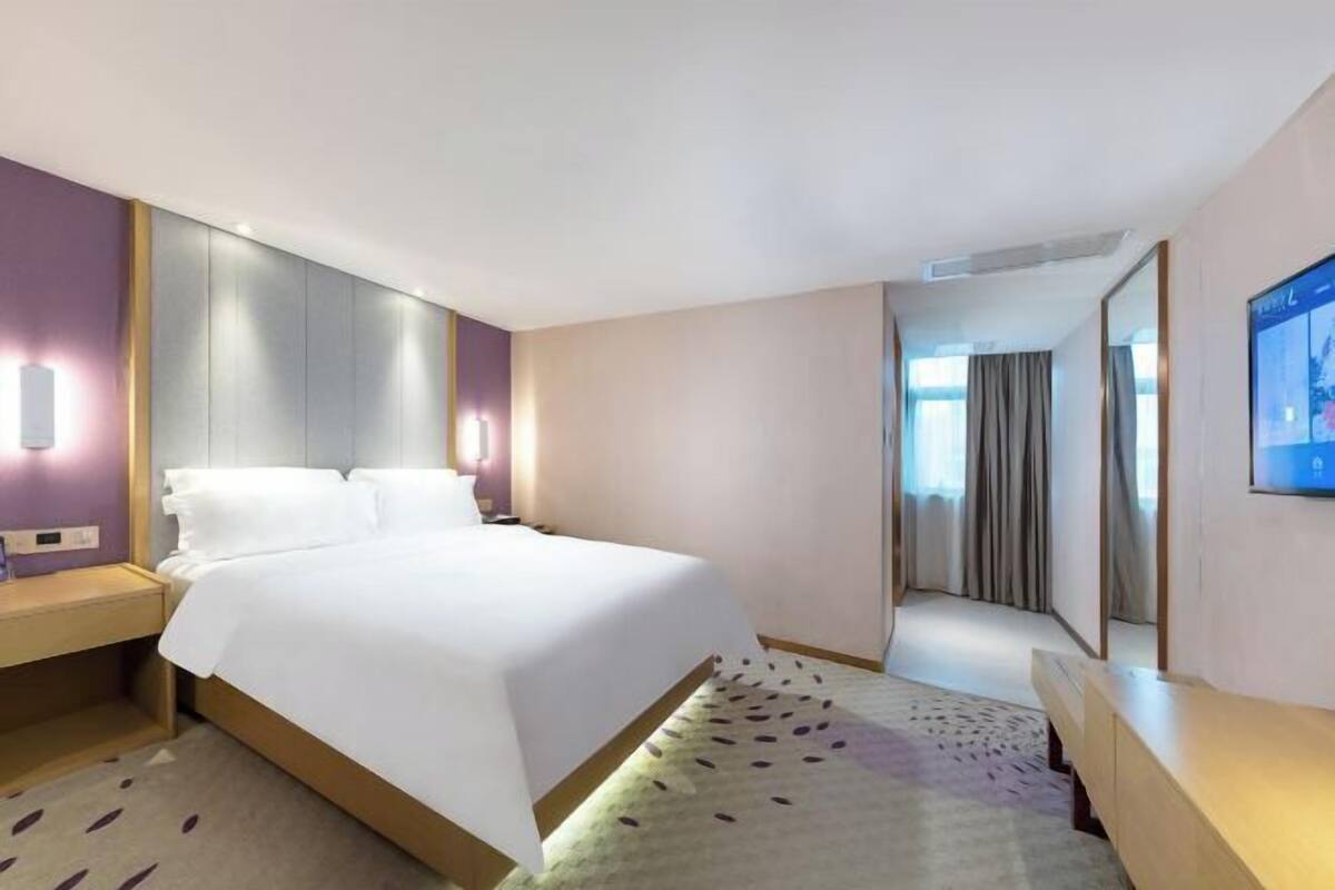 Ein Hotelzimmer mit einem großen Bett, einem Nachttisch, einem an der Wand befestigten Fernseher und einem Spiegel.
