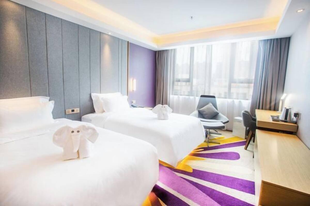 Ein Hotelzimmer mit zwei Betten, einem Schreibtisch, einem Stuhl und einem großen Fenster mit Vorhängen.