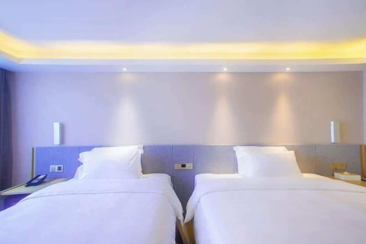 A hotel room with two beds, a nightstand with a phone, and a wall-mounted light fixture.