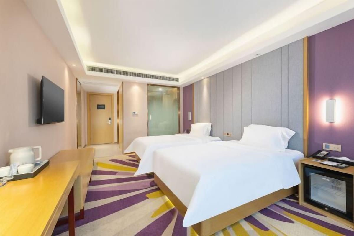A hotel room with two beds, a desk, a television, and a minibar.
