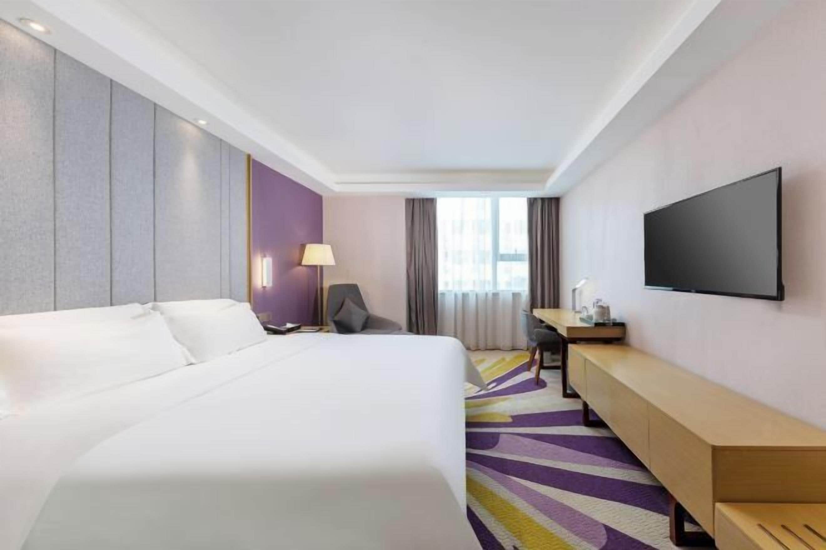 Une chambre d’hôtel avec un lit, un bureau, une chaise, une télévision et une fenêtre avec des rideaux.