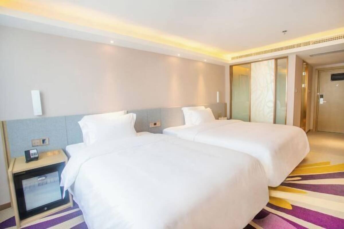 Ein Hotelzimmer mit zwei Betten, einem Nachttisch mit Telefon und einem großen Spiegel.