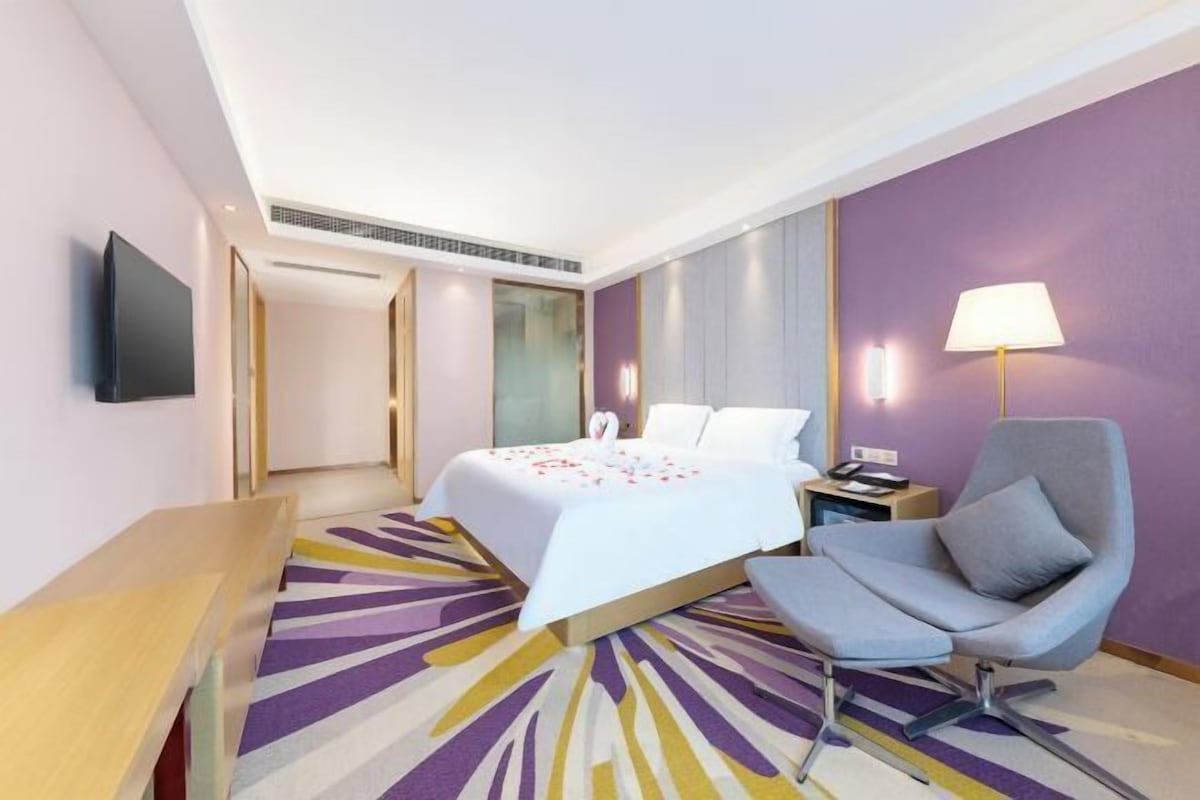 A hotel room with a bed, a desk, a chair, a TV, and a lamp.