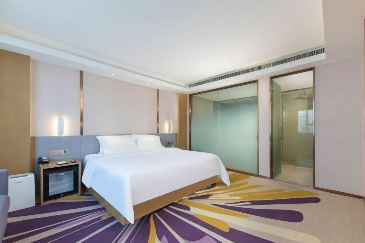 A hotel room with a large bed, a desk with a computer, a small TV, and a glass shower enclosure.