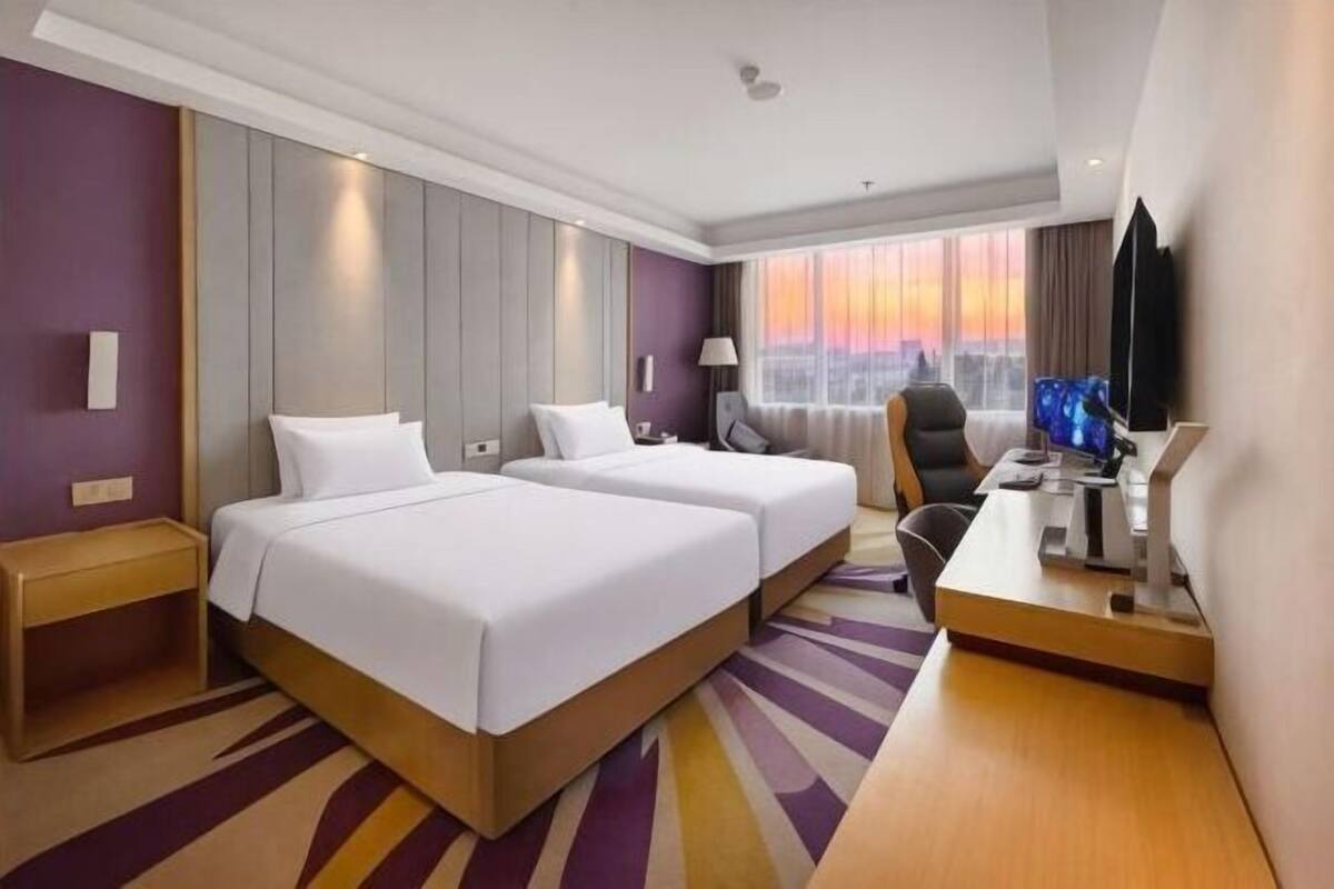 Ein Hotelzimmer mit zwei Betten, einem Schreibtisch, einem Sessel, einem Fernseher und einem Fenster mit Blick.