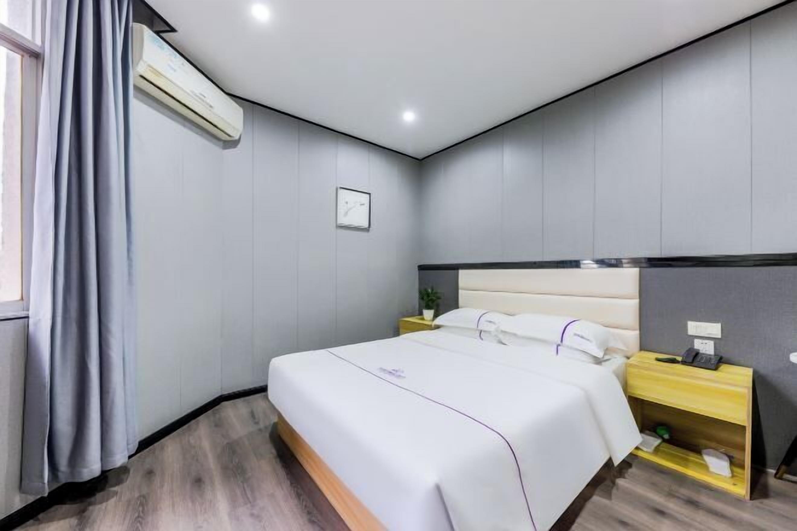 Una habitación de hotel moderna con una cama grande, mesitas de noche, un equipo de aire acondicionado y una ventana con cortinas.