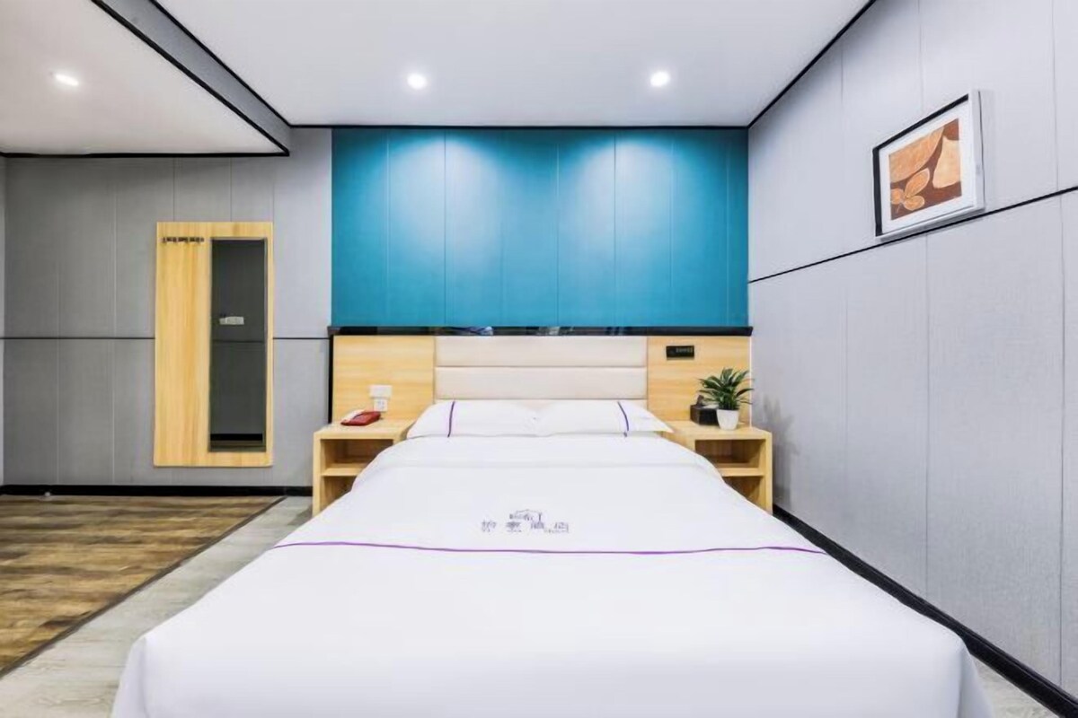 A hotel room with a bed, a nightstand, a bedside table, a wooden wardrobe, and a blue accent wall.