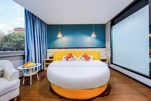 A modern hotel room with a large bed, a small round table with fruit, a white armchair, and a large window with curtains. - Yijia Hotel (Ji'an No.2 Middle School Pedestrian Street) (Ji'an)