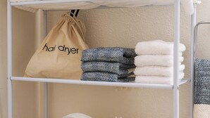 Un étendoir métallique avec des serviettes pliées et un sac étiqueté « sèche-cheveux » dans une salle de bain.