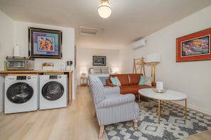 Un espace de vie compact comprenant un lave-linge, un canapé, une petite table et un lit avec une tête de lit.